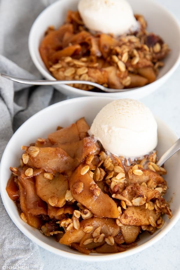 close-up of a serving of healthy apple crisp in a white bowl served with vanilla ice cream