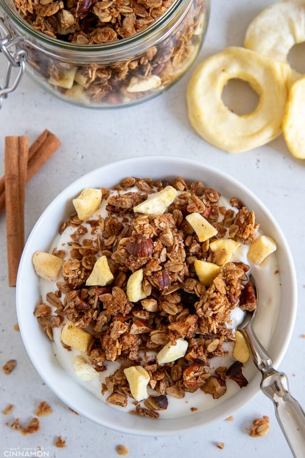 apple pie granola sprinkled on greek yogurt with a spoon on the side 