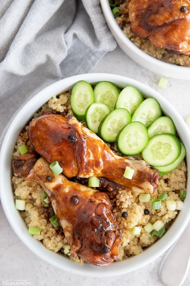 a serving of chicken adobo - two drumsticks on a bed of quinoa with cucumber salad as a side 