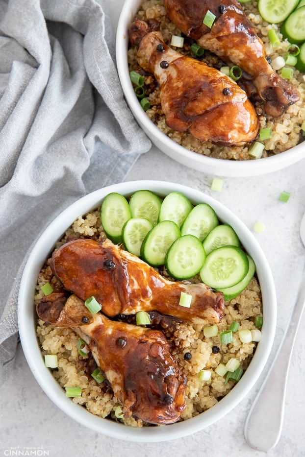 overhead shot of two chicken adobo bowls with chicken drumsticks on quinoa and sliced cucumbers