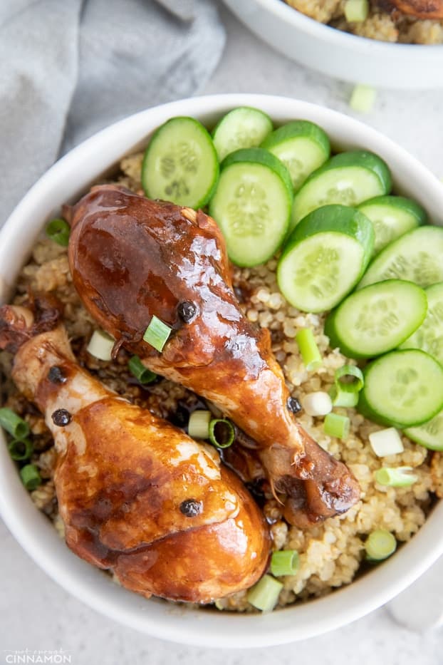 a bowl of chicken adobo resting on a bed of quinoa with cucumber salad on the side