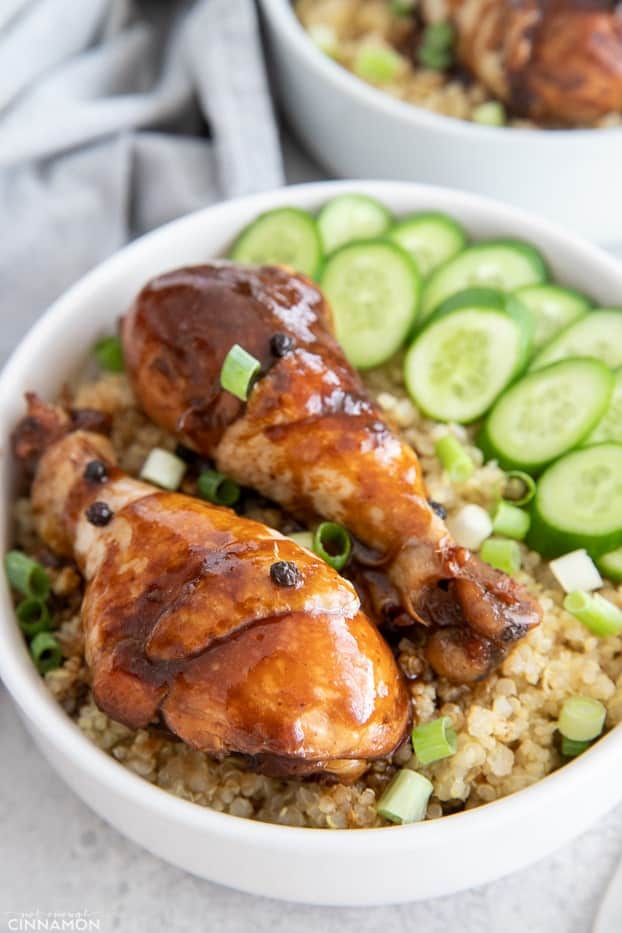 two chicken adobo drumsticks resting on a bed of quinoa with a side of cucumber salad presented as a bowl