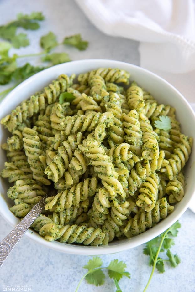 closeup of a bowl of creamy cilantro pasta tossed with rotini pasta with a fork and fresh cilantro