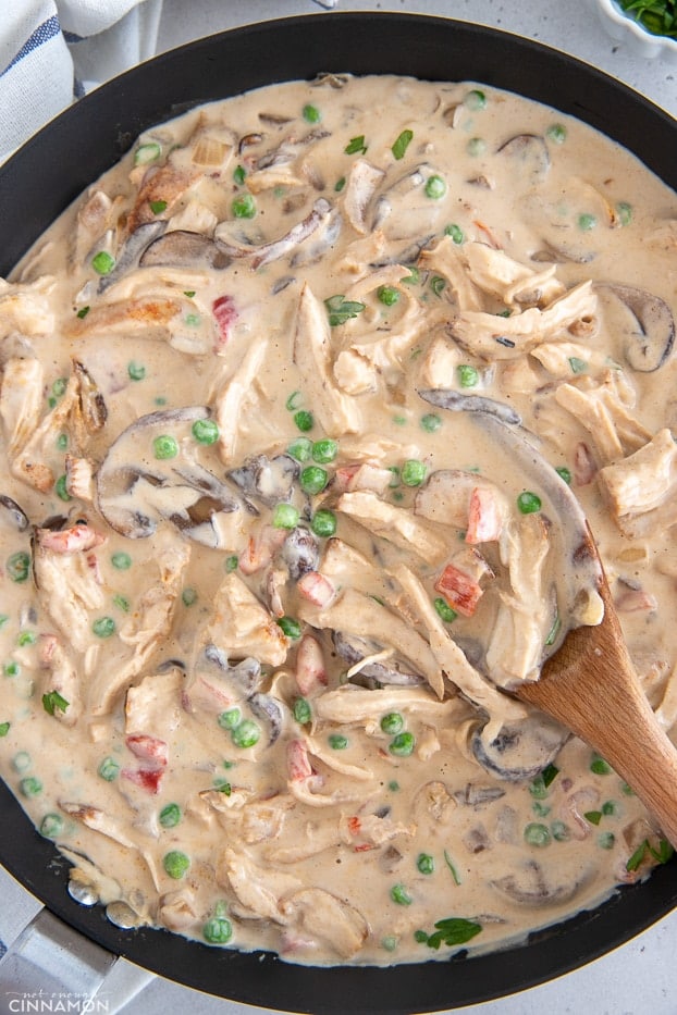 overhead shot of a skillet with creamy dairyfree chicken a la king with a wooden spoon