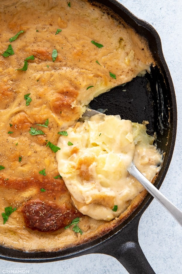 a black skillet with vegan scalloped potatoes with a spoon taking out one serving