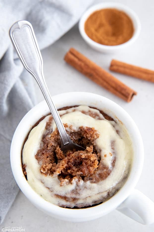 a spoon being dug into a mug with healthy cinnamon roll mug cake 