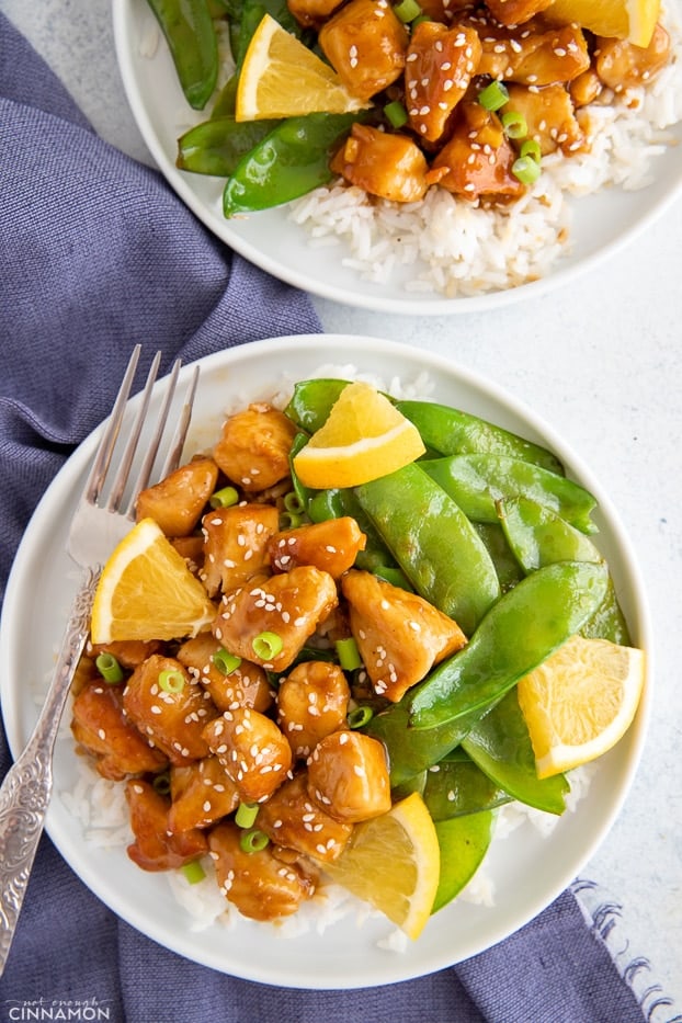 overhead shot of Chinese orange chicken served over rice with a side of snow peas 