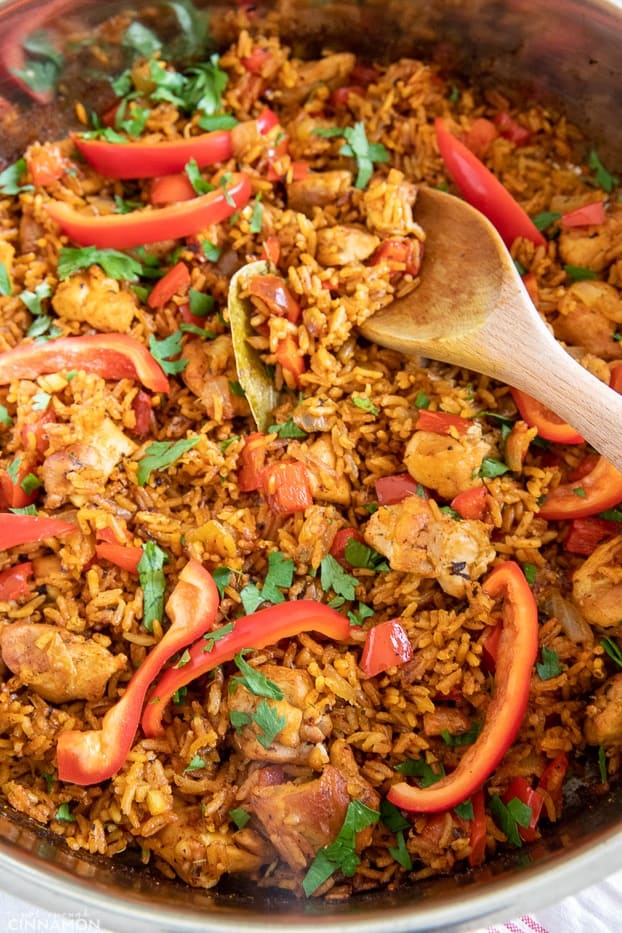 a wooden spoon stirring in a pot of homemade West African Jollof chicken and rice 