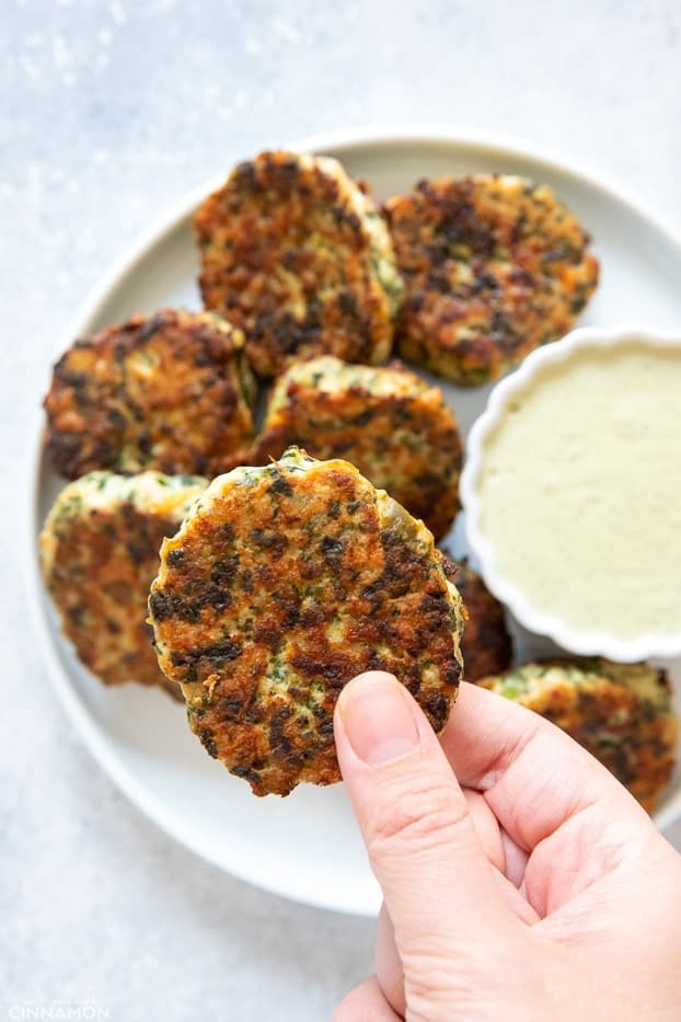 a hand holding a paleo chicken popper over a plate of chicken poppers and dip 