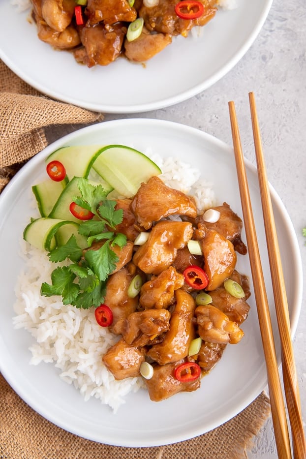 a serving of coconut caramel chicken with rice and cucumber salad with chopsticks on the side 