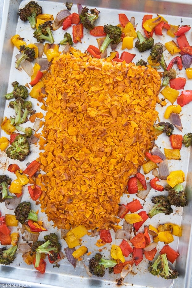 a sheet pan with a potato chips crusted salmon fillet surrounded by vegetables