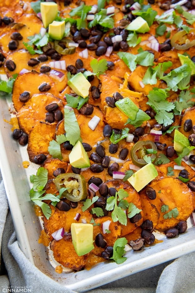 healthy sweet potato nachos on a sheet pan topped with avocado and black beans