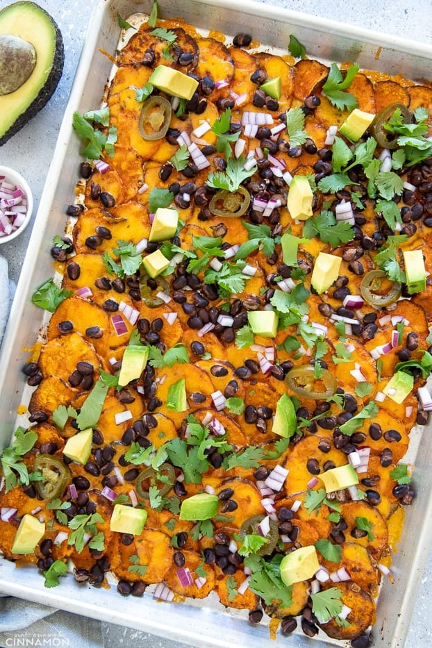 a sheet pan with loaded baked sweet potato nachos with avocado, cilantro and onion 