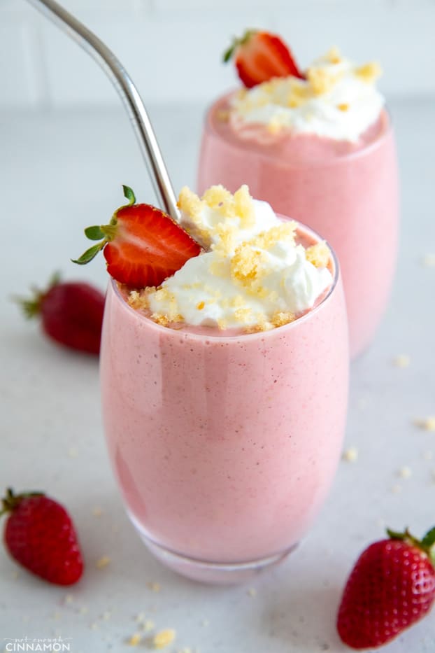 strawberry shortcake protein shake served in a 2 tall glasses topped with a swirl of whipped cream and cake crumbs