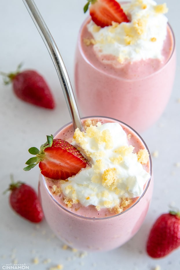 healthy strawberry shortcake protein shake served in a tall glass topped with a swirl of whipped cream and cake crumbs