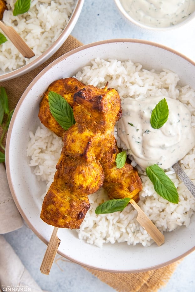 overhead shot of a bowl with rice topped with tandoori chicken skewers