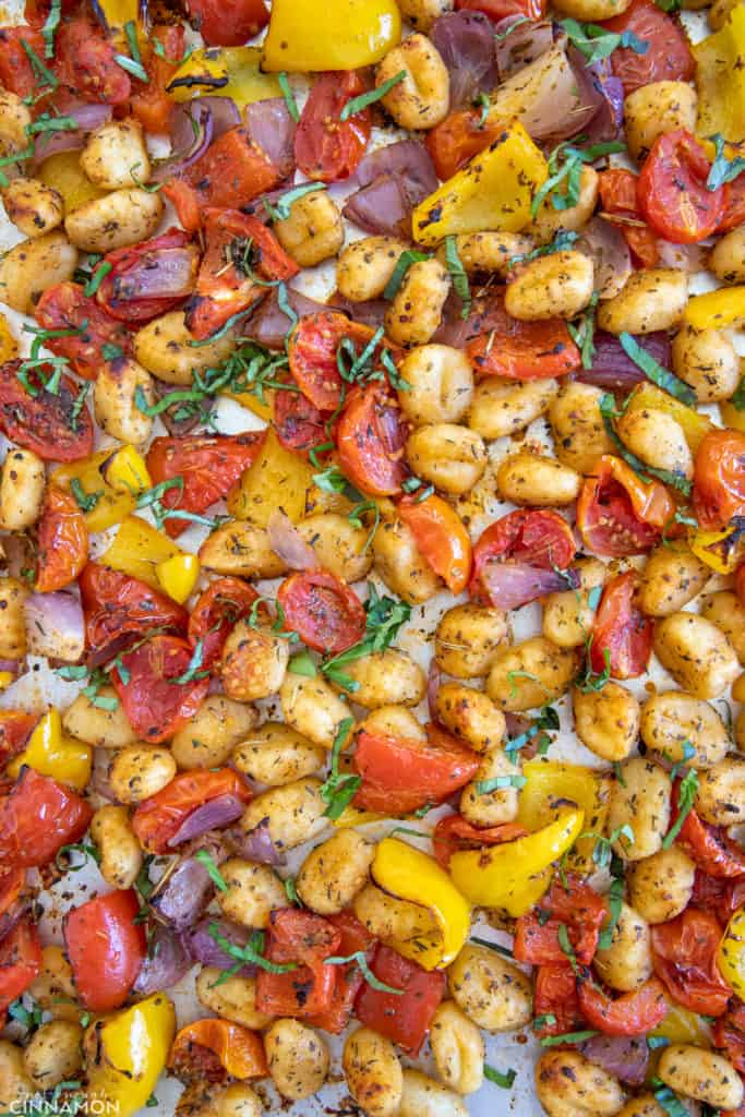 overhead shot of a sheet pan with crispy baked gnocchi and roasted vegetables sprinkled with fresh basil