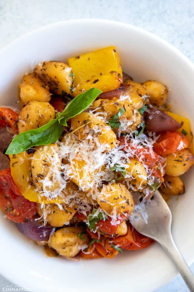 a bowl with crispy sheet pan gnocchi with roasted vegetables served in a bowl with grated parmesan cheese