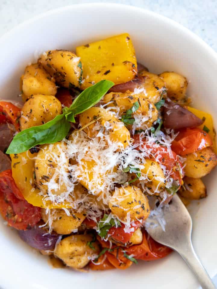 a small bowl with crispy sheet pan gnocchi with roasted vegetables served with grated parmesan and basil