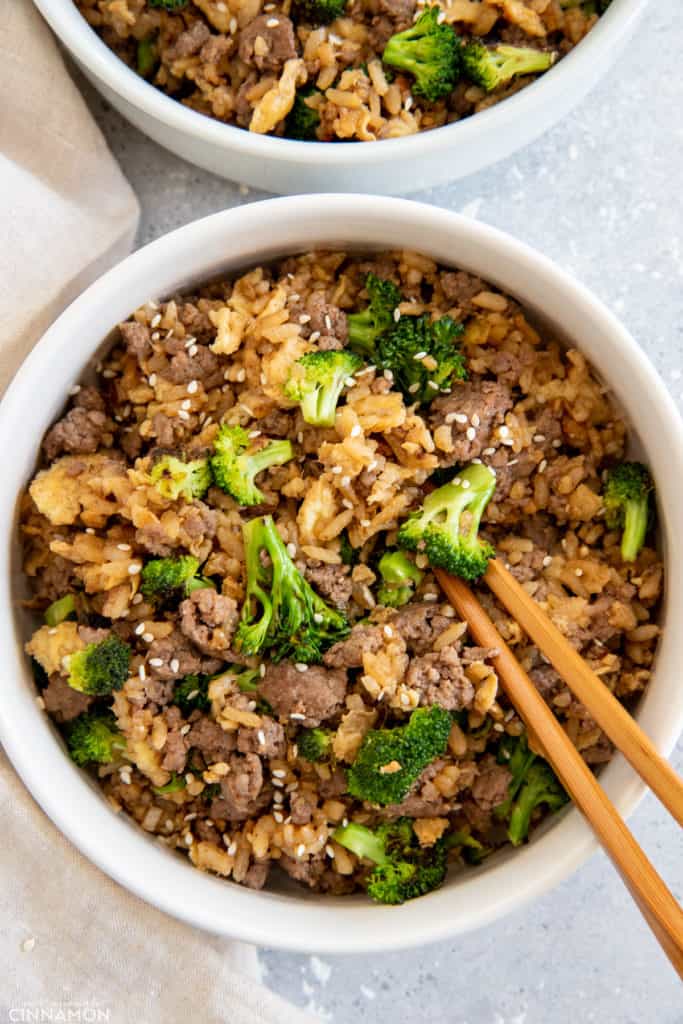 two servings of Mongolian Beef and broccoli fried rice served in bowls with chopsticks