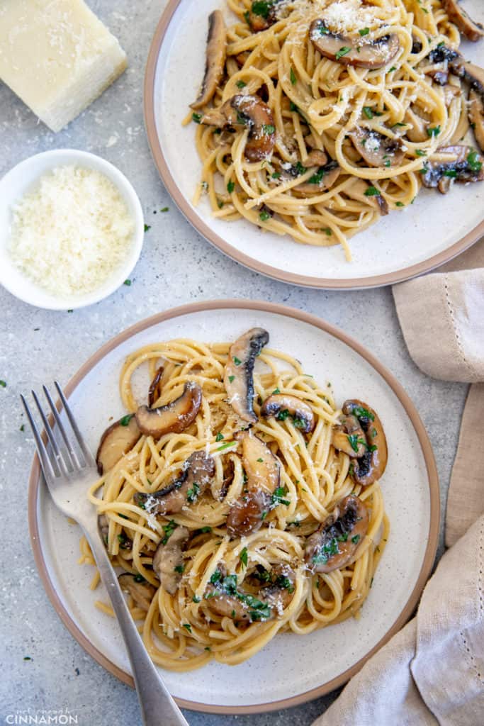 mushroom carbonara served on two plated garnished with parsley and grated pecorino