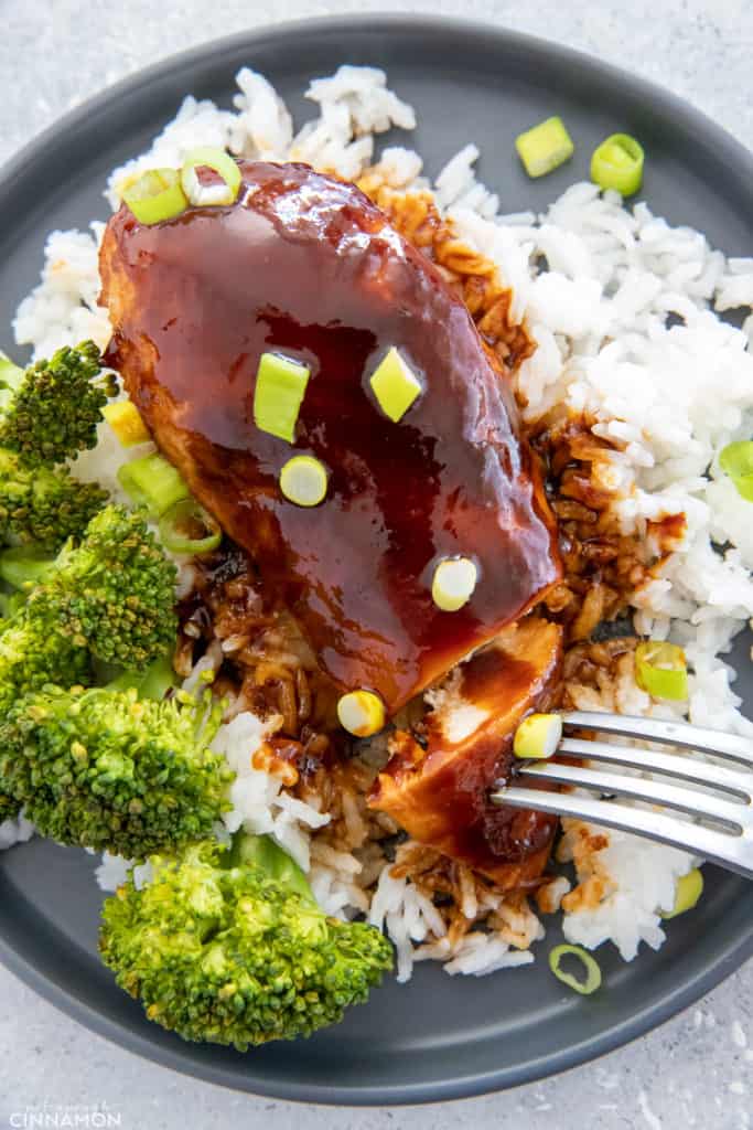 a fork reaching for a slice of baked firecracker chicken breast served on a bed of rice