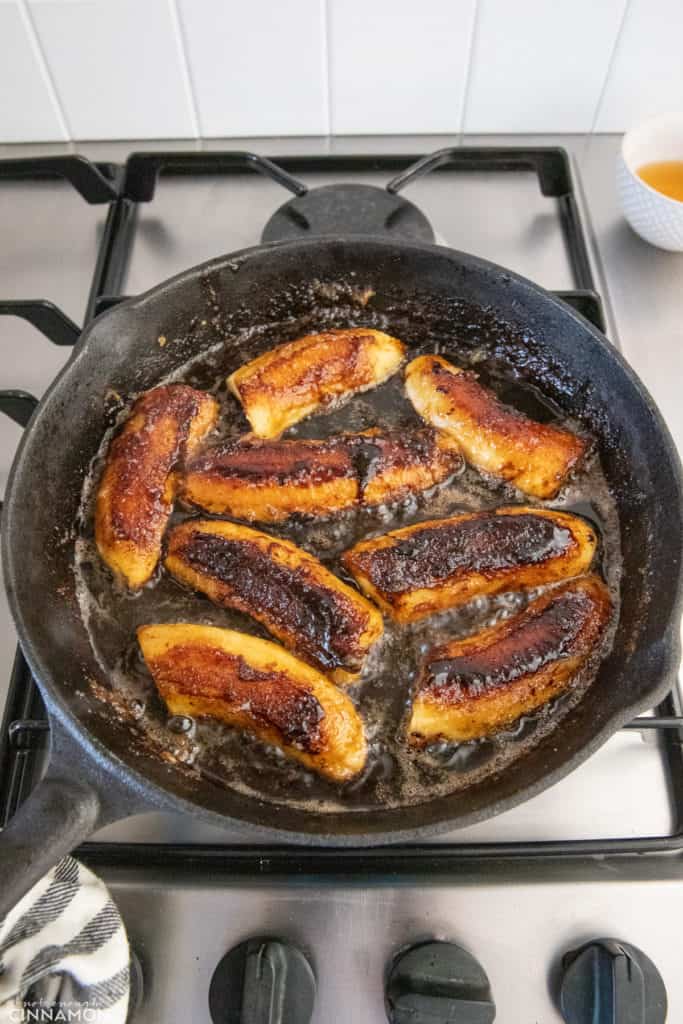 banana slices simmering in rum caramel sauce in a black skillet 